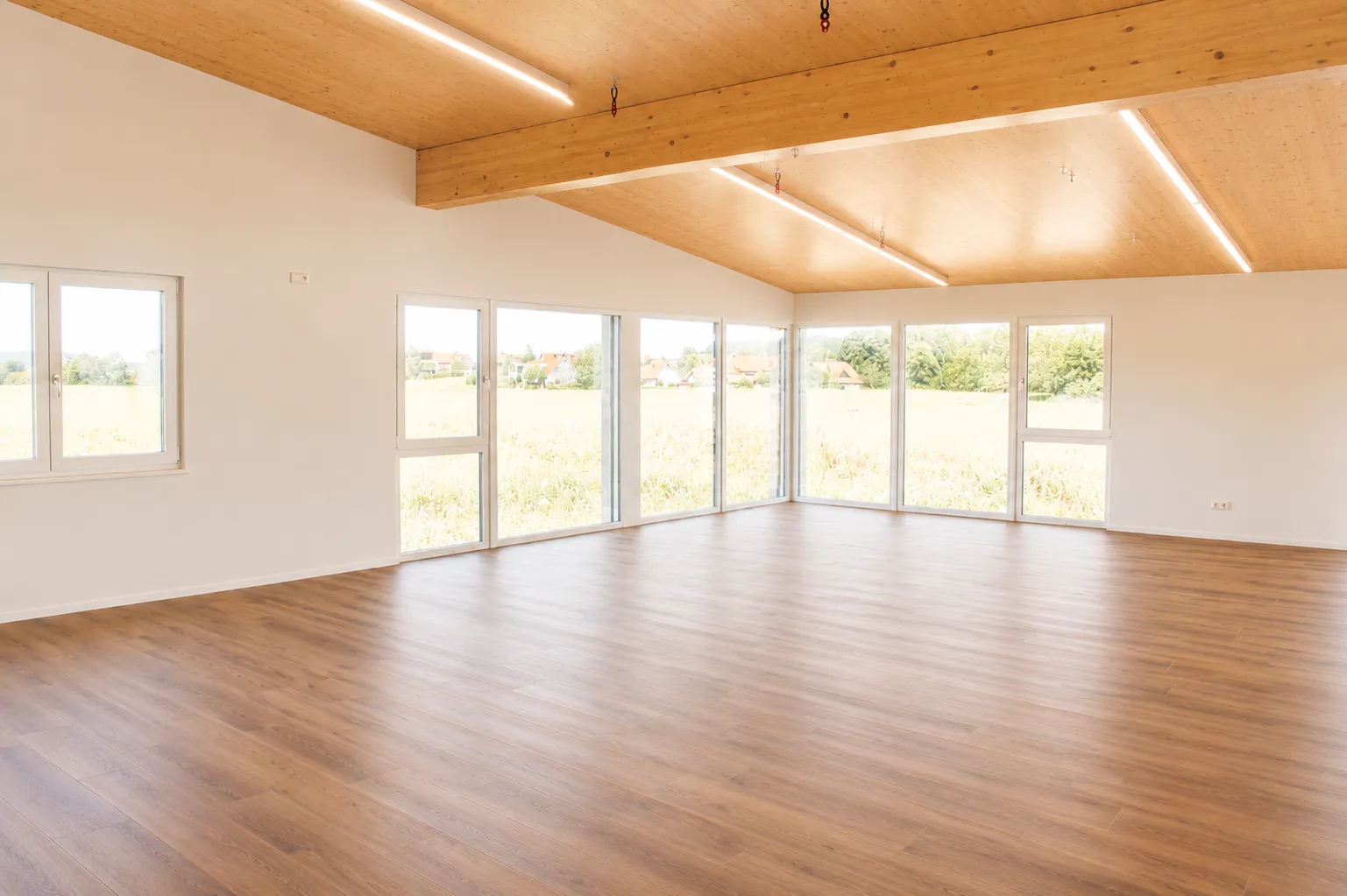 Der helle Tanzsaal mit großer Fensterfront, weitem Holzboden und sichtbarer Holzdecke.