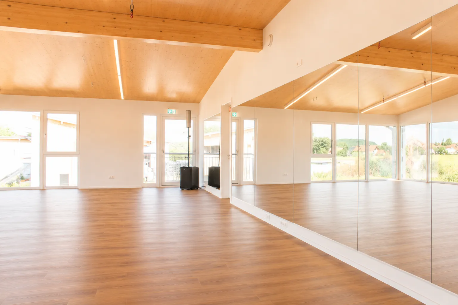 Die raumhohe Spiegelwand des Saals, in der sich Fensterfront, Holzboden und Holzdecke spiegeln.
