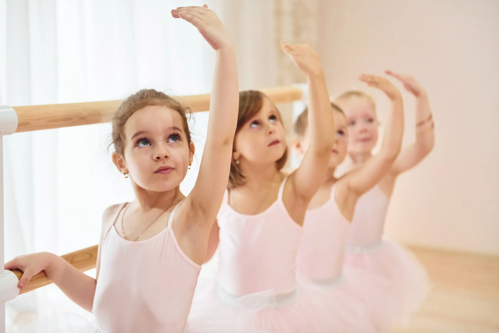 Vier kleine Mädchen an der Ballettstange heben gemeinsam einen Arm über den Kopf.