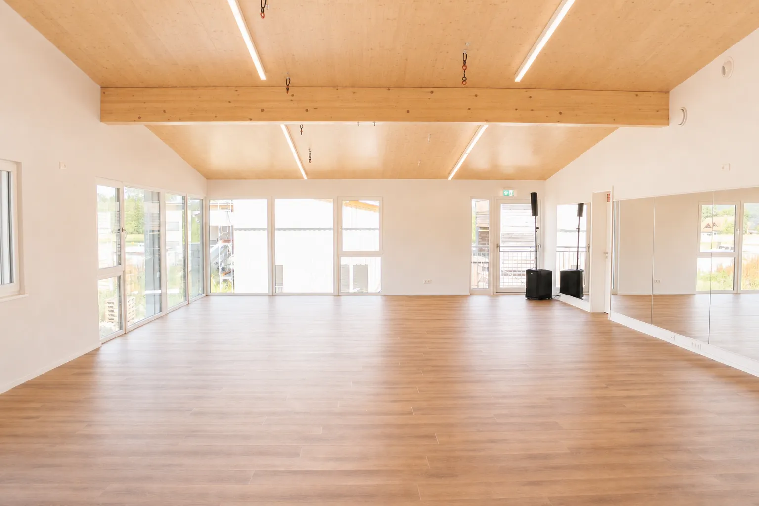 Der leere Tanzsaal in ganzer Breite mit Holzboden, heller Fensterfront, Holzdecke und Spiegelwand.